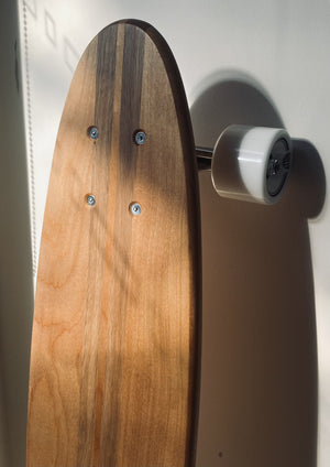 Handmade timber skateboard, drenched in sunlight against a white wall