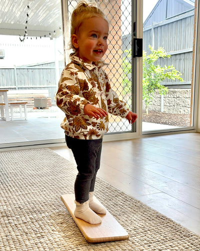 Child standing on a balance board indoors with a sliding glass door in the background